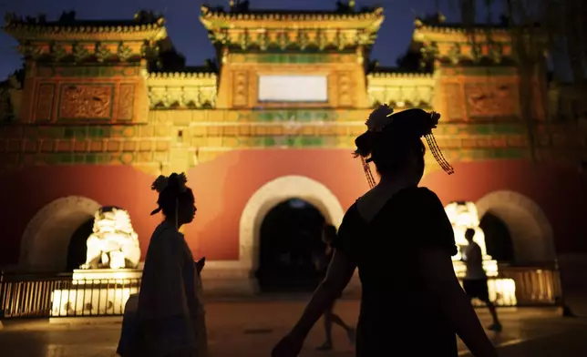 Chinese women dressed in Qing Dynasty attire walk in front of a traditional gate at Beihai park in Beijing, China, Sunday, July 28, 2024. (AP Photo/Vincent Thian)