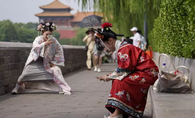 A Chinese girl dressed in Qing Dynasty attire takes photographs of another near the Forbidden city in Beijing, China, Sunday, July 21, 2024. (AP Photo/Vincent Thian)