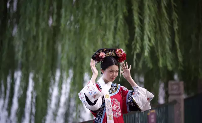 A Chinese woman dressed in Qing Dynasty attire and headdress stands for a photograph at Beihai park in Beijing, China, Sunday, July 28, 2024. (AP Photo/Vincent Thian)