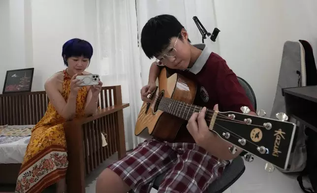 Chinese mother Jiang Wenhui, left, records her son Rodney Feng playing the acoustic guitar in Chiang Mai province, Thailand, Tuesday, April 23, 2024.(AP Photo/Sakchai Lalit)