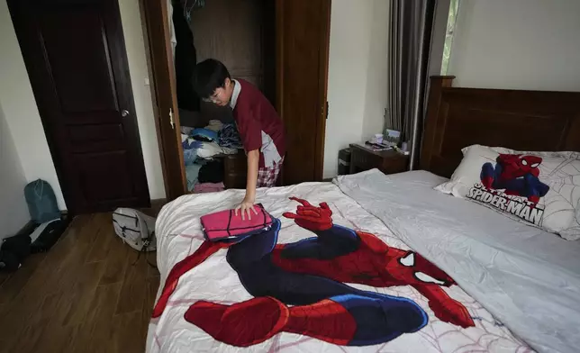 Rodney Feng arranges his clothes after returning from school in Chiang Mai province, Thailand, Tuesday, April 23, 2024. (AP Photo/Sakchai Lalit)