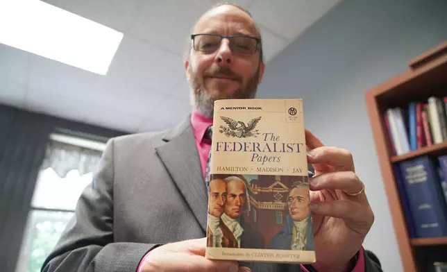 Professor Wade Maki holds up a copy of the book "The Federalist Papers" in his office in Greensboro, N.C., on Wednesday, April 24, 2024. Maki, chairman of the University of North Carolina system's faculty senate, helped draft a civics requirement that students at all publicly funded colleges will have to fulfill starting in July 2025. (AP Photo/Allen G. Breed)