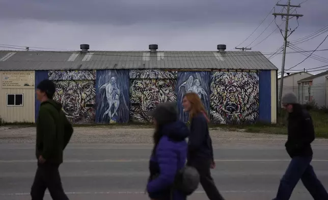 People walk near a mural on the side of a local tourism company, Monday, Aug. 5, 2024, in Churchill, Manitoba. (AP Photo/Joshua A. Bickel)