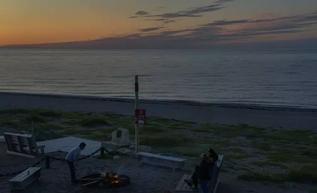 People start a bonfire at sunset next to a sign warning them of polar bears, Saturday, Aug. 3, 2024, in Churchill, Manitoba. (AP Photo/Joshua A. Bickel)