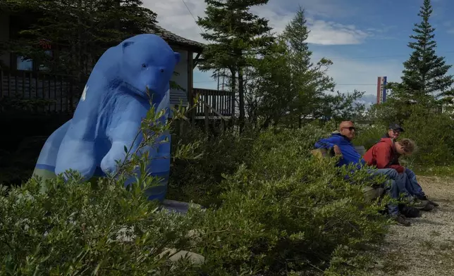 Tourists sit near a polar bear statue, Tuesday, Aug. 6, 2024, in Churchill, Manitoba. (AP Photo/Joshua A. Bickel)