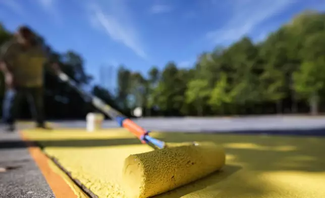 Ronnie Jefferies paints the parking lot at Science, Arts and Entrepreneurship School to help cool it by making it more reflective, Wednesday, Sept. 4, 2024, in Mableton, Ga. (AP Photo/Mike Stewart)