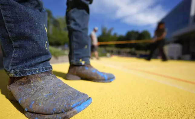 Ronnie Jefferies works on the parking lot at Science, Arts and Entrepreneurship School where it is being repainted to help cool it by making it more reflective, Wednesday, Sept. 4, 2024, in Mableton, Ga. (AP Photo/Mike Stewart)