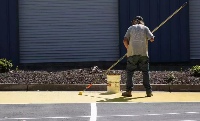 Ronnie Jefferies paints the parking lot at Science, Arts and Entrepreneurship School to help cool it by making it more reflective, Wednesday, Sept. 4, 2024, in Mableton, Ga. (AP Photo/Mike Stewart)