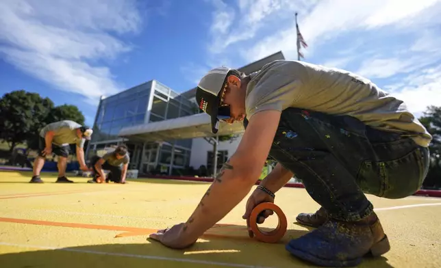 Ronnie Jefferies works on the parking lot at Science, Arts and Entrepreneurship School where it is being repainted to help cool it by making it more reflective, Wednesday, Sept. 4, 2024, in Mableton, Ga. (AP Photo/Mike Stewart)