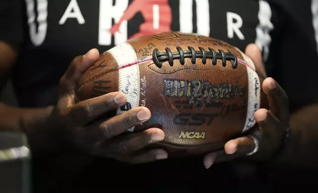 Phillip Laster Sr. holds a football in Brandon, Miss., Tuesday, Aug. 27, 2024, signed by teammates of his son Phillip Laster Jr., that was given to him on senior night after his passing. (AP Photo/Gerald Herbert)