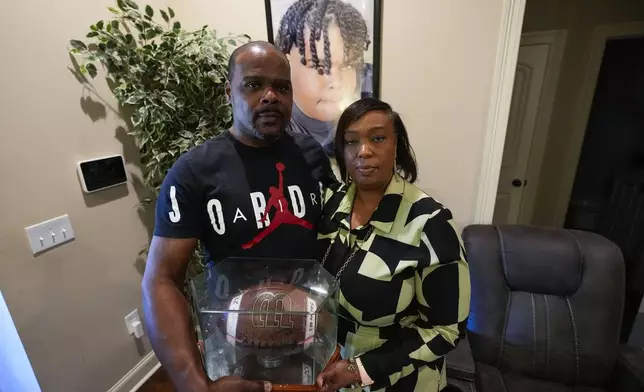 Phillip Laster Sr. and his wife Ashanta Laster hold a football signed by teammates of their son Phillip Laster Jr., in Brandon, Miss., Tuesday, Aug. 27, 2024, that was given to them on senior night after Laster Jr.'s passing. A portrait of Laster Jr. is behind them. (AP Photo/Gerald Herbert)