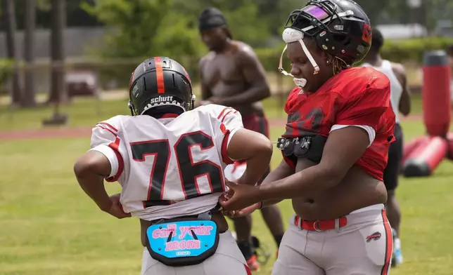 Keiland Burns, left, wears a protective pad that reads "call your mom" as teammate Jamie Allen, right, helps him with his gear at the start of football practice at Baker High in Baker, La., Wednesday, Aug. 28, 2024. (AP Photo/Gerald Herbert)