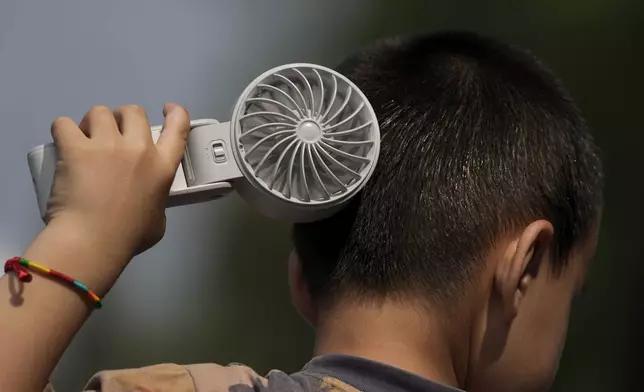 FILE - A boy cools himself with an electric fan on a sweltering day at a park in Tongzhou, on the outskirts of Beijing, Monday, June 10, 2024. (AP Photo/Andy Wong)