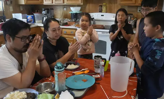 Bosco and Jennifer Carl say grace with their children before a meal at their home on Saturday, Aug. 17, 2024, in Mertarvik, Alaska. (AP Photo/Rick Bowmer)