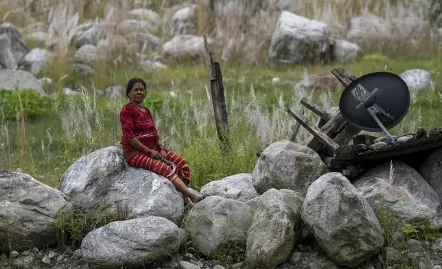 Suntali Jyoti, 56, sits where her house and field once stood, in Chanaute, Melamchi, northeast from Kathmandu, Nepal, Sunday, Sept. 15, 2024, now covered with large rocks brought by floods in 2021. (AP Photo/Niranjan Shrestha)