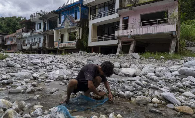 A man sets a fish trap near homes abandoned after flooding at Chanaute Market, Melamchi, northeast of Kathmandu, Nepal, on Sunday, Sept. 15, 2024. (AP Photo/Niranjan Shrestha)