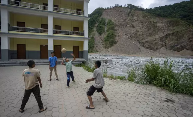 Children play volleyball with a landslide-damaged hill visible in the background at Saraswati Secondary School in Gyalthum, Melamchi, northeast of Kathmandu, Nepal on Saturday, Sept. 14, 2024. (AP Photo/Niranjan Shrestha)