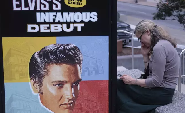 Sandra Morris sits outside the Ryman plaza next to a poster of commemorating a performance by Elvis Presley at the concert venue in Nashville, Tenn., on July 30, 2024. (AP Photo/Luis Andres Henao)