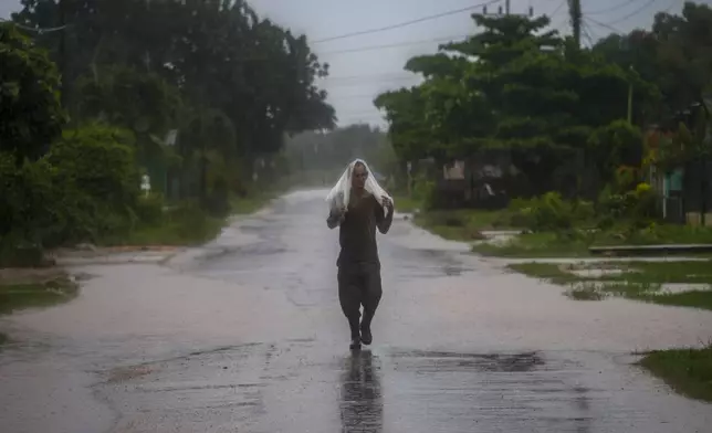 A resident uses a piece of plastic as protection from heavy rains brought on by Hurricane Helene, in Batabano, Cuba, Wednesday, Sept. 25, 2024. (AP Photo/Ramon Espinosa)