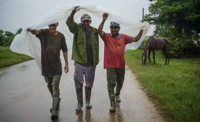 Residents use a piece of plastic as protection from heavy rains brought on by Hurricane Helene, in Batabano, Cuba, Wednesday, Sept. 25, 2024. (AP Photo/Ramon Espinosa)