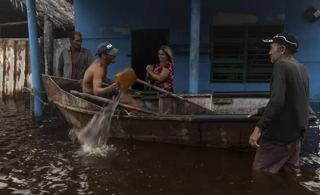 A man removes water from a boat while talking to neighbors after the passage of Hurricane Helene in Guanimar, Artemisa province, Cuba, Wednesday, Sept. 25, 2024. (AP Photo/Ramon Espinosa)