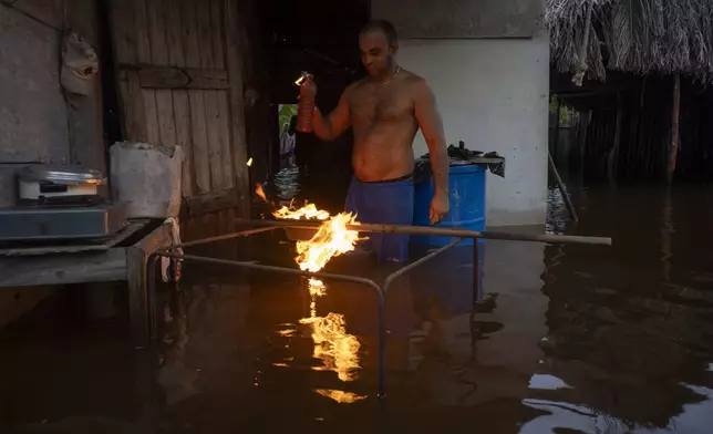 A man lights charcoal to cook dinner in his flooded home after the passage of Hurricane Helene in Guanimar, Artemisa province, Cuba, Wednesday, Sept. 25, 2024. (AP Photo/Ramon Espinosa)