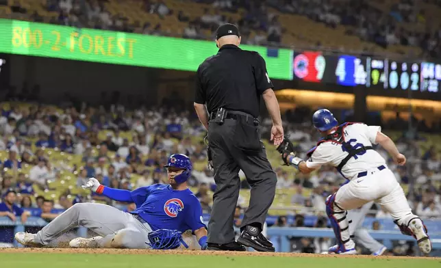 Chicago Cubs' Seiya Suzuki, left, scores on a sacrifice fly by Isaac Paredes as Los Angeles Dodgers catcher Will Smith, right, takes a late throw and home plate umpire Todd Tichenor washes during the ninth inning of a baseball game, Monday, Sept. 9, 2024, in Los Angeles. (AP Photo/Mark J. Terrill)