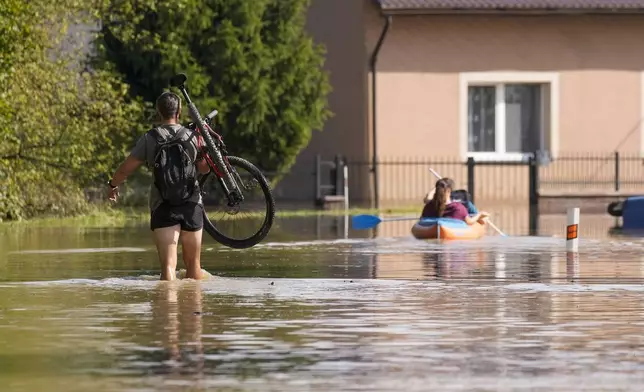 A resident carries his bicycle as others paddle through a flooded street in Bohumin, Czech Republic, Tuesday, Sept. 17, 2024. (AP Photo/Darko Bandic)