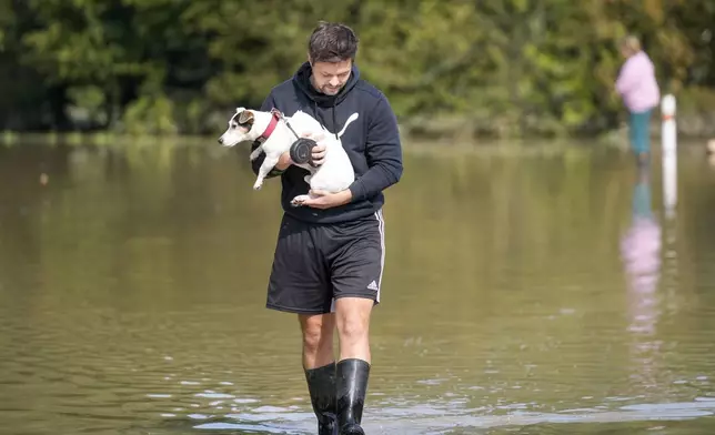 Radek Dan carries his dog through his flooded neighbourhood in Bohumin, Czech Republic, Tuesday, Sept. 17, 2024. (AP Photo/Darko Bandic)