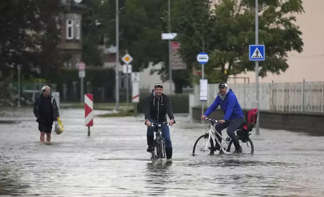 Residents ride bicycles through a flooded street in Litovel, Czech Republic, Monday, Sept. 16, 2024. (AP Photo/Petr David Josek)