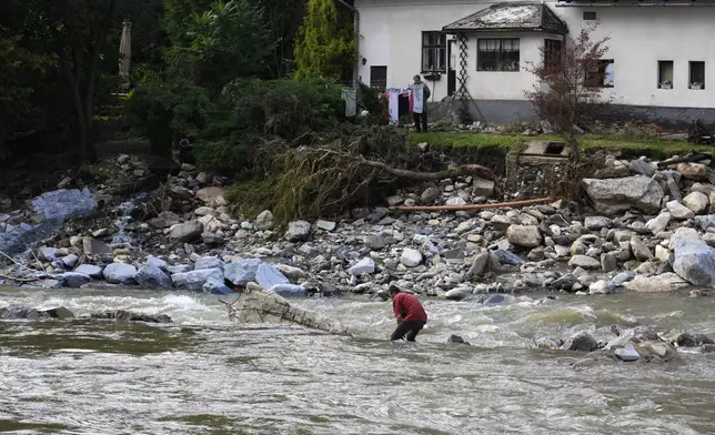 A man walks cross a river as residents return to clean up after recent floods near Pisecna, Czech Republic, Thursday, Sept. 19, 2024. (AP Photo/Petr David Josek)