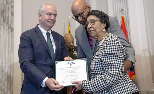 Sen. Chris Van Hollen, D-Md., left, presents the Distinguished Service Cross Award to Joann Woodson, center, and her son Steve Woodson, right, during a ceremony to posthumously award the Distinguished Service Cross to her husband U.S. Army Staff Sgt. Waverly Woodson, Jr., a medic who was part of the only Black combat unit to take part in the D-Day invasion of France during World War II, on Capitol Hill, in Washington, Tuesday, Sept. 24, 2024. (AP Photo/Rod Lamkey, Jr.)