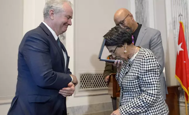 Joann Woodson, center, kisses the Distinguished Service Cross while Sen. Chris Van Hollen, D-Md., left, and her son Steve Woodson, right, watch during a ceremony to posthumously award the Distinguished Service Cross to her husband U.S. Army Staff Sgt. Waverly Woodson, Jr., a medic who was part of the only Black combat unit to take part in the D-Day invasion of France during World War II, on Capitol Hill, in Washington, Tuesday, Sept. 24, 2024. (AP Photo/Rod Lamkey, Jr.)