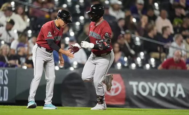 Arizona Diamondbacks third base coach Tony Perezchica, left, congratulates Christian Walker as he circles the bases after hitting a solo home urn off Colorado Rockies relief pitcher Jaden Hill in the eighth inning of a baseball game Tuesday, Sept. 17, 2024, in Denver. (AP Photo/David Zalubowski)