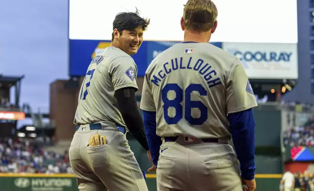 Los Angeles Dodgers two-way player Shohei Ohtani, left, shares a laugh with first base coach Clayton McCullough, right, before he takes the field after the National Anthem in the xxxx inning of a baseball game against the Atlanta Braves, Saturday, Sept. 14, 2024, in Atlanta. (AP Photo/Jason Allen)