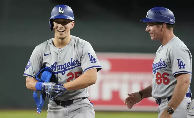 Los Angeles Dodgers' Tommy Edman, left, smiles as he celebrates his two-run single against the Arizona Diamondbacks with Dodgers first base coach Clayton McCullough (86) during the ninth inning of a baseball game Saturday, Aug. 31, 2024, in Phoenix. (AP Photo/Ross D. Franklin)