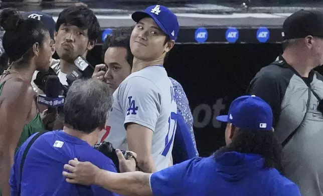 Los Angeles Dodgers' Shohei Ohtani, of Japan, smiles at teammates as he does a postgame interview after a baseball game against the Miami Marlins, Thursday, Sept. 19, 2024, in Miami. (AP Photo/Wilfredo Lee)