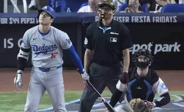 Los Angeles Dodgers' Shohei Ohtani, left, of Japan, watches the ball as he hits a home run, scoring Max Muncy and Chris Taylor, during the ninth inning of a baseball game against the Miami Marlins, Thursday, Sept. 19, 2024, in Miami. (AP Photo/Wilfredo Lee)