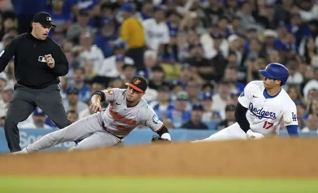 Los Angeles Dodgers' Shohei Ohtani, right, is hit by a ball thrown from home plate as he steals third while Baltimore Orioles third baseman Ramon Urias misses the ball and third base umpire Jansen Visconti watches during the third inning of a baseball game Wednesday, Aug. 28, 2024, in Los Angeles. (AP Photo/Mark J. Terrill)