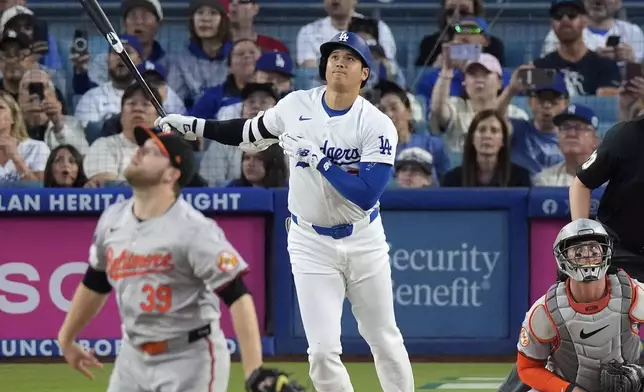 Los Angeles Dodgers' Shohei Ohtani, center, hits a solo home run as Baltimore Orioles starting pitcher Corbin Burnes, left, and catcher James McCann, right, watch during the first inning of a baseball game Wednesday, Aug. 28, 2024, in Los Angeles. (AP Photo/Mark J. Terrill)