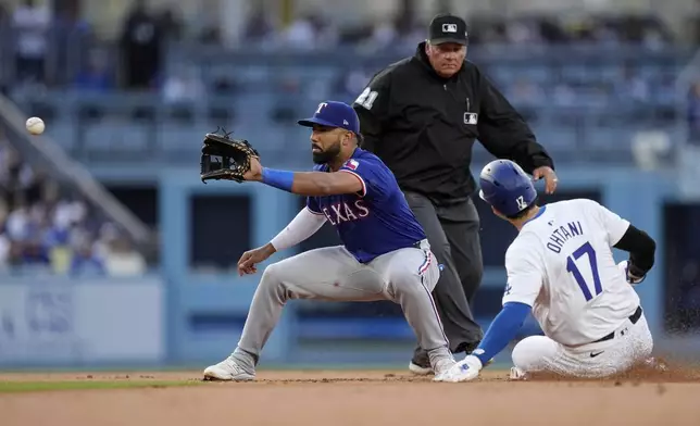 Los Angeles Dodgers' Shohei Ohtani, right, steals second as Texas Rangers shortstop Ezequiel Duran, left, takes a late throw while second base umpire Hunter Wendelstedt watches during the first inning of a baseball game Tuesday, June 11, 2024, in Los Angeles. (AP Photo/Mark J. Terrill)