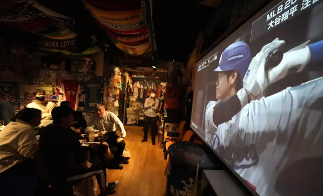 People watch Los Angeles Dodgers' Shohei Ohtani batting on a television live broadcasting a MLB opening game between the San Diego Padres and Los Angeles Dodgers, at a sports bar in Tokyo, Wednesday, March 20, 2024. (AP Photo/Shuji Kajiyama)