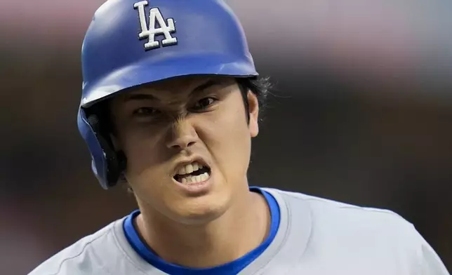 Los Angeles Dodgers' Shohei Ohtani, right, grimaces after hitting a single as he stands on first base during the third inning of a baseball game against the San Diego Padres, Friday, May 10, 2024, in San Diego. (AP Photo/Gregory Bull)