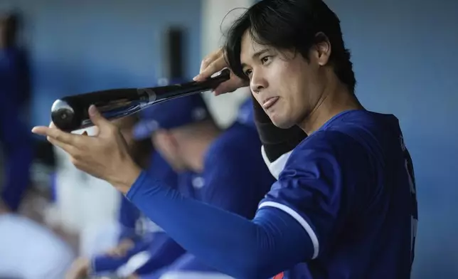 Los Angeles Dodgers' Shohei Ohtani eyes his bat in the dugout before a spring training baseball game against the Cincinnati Reds on Friday, March 8, 2024, in Phoenix. (AP Photo/Carolyn Kaster)