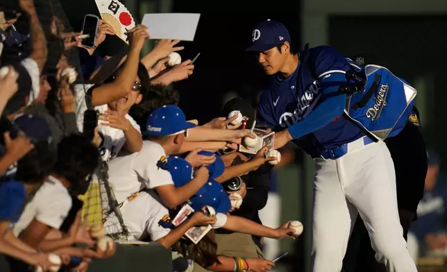 Los Angeles Dodgers designated hitter Shohei Ohtani signs autographs for fans before a spring training baseball game against the Cleveland Guardians in Phoenix, Friday, March 1, 2024. (AP Photo/Ashley Landis)