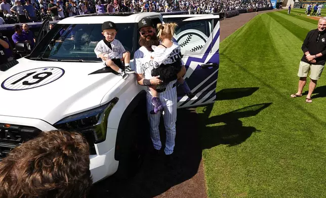 Colorado Rockies center fielder Charlie Blackmon, center, holds his 3-year-old daughter Josie, while his 2-year-old son Wyatt, sits on the hood of a pickup truck given to Blackmon during a ceremony to mark his retirement after 14 seasons as a member of the team before a baseball game against the Los Angeles Dodgers, Sunday, Sept. 29, 2024, in Denver. (AP Photo/David Zalubowski)