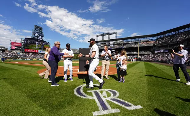 Colorado Rockies center fielder Charlie Blackmon, center, greets, from front left to right, general manager Bill Schmidt, manager Bub Black and team co-owner Dick Monfort while Blackmon's wife, Ashley, looks on with their children, 3-year-old Josie and 2-year-old Wyatt, during a ceremony to mark his retirement after 14 seasons as a member of the team before a baseball game against thee Los Angeles Dodgers, Sunday, Sept. 29, 2024, in Denver. (AP Photo/David Zalubowski)