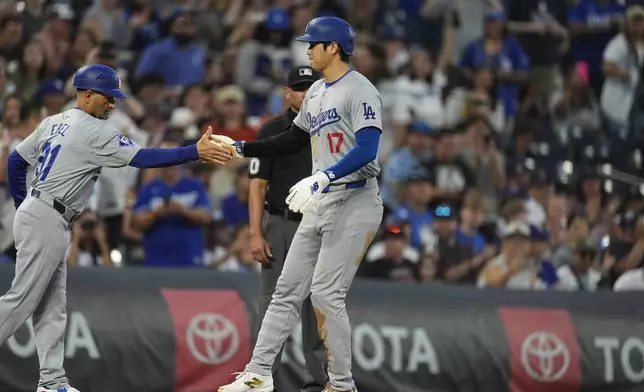 Los Angeles Dodgers third base coach Dino Ebel, left, congratulates Shohei Ohtani after he stole second base and then advance to third base on a throwing error by Colorado Rockies catcher Jacob Stallings in the second inning of a baseball game, Friday, Sept. 27, 2024, in Denver. (AP Photo/David Zalubowski)