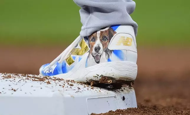 Decoy, the dog of Los Angeles Dodgers two-way player Shohei Ohtani, adorns the spike of Ohtani as he steps on first base after hitting an RBI single off Colorado Rockies starting pitcher Cal Quantrill in the second inning of a baseball game, Friday, Sept. 27, 2024, in Denver. (AP Photo/David Zalubowski)