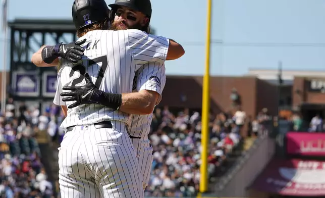 Colorado Rockies pinch-runner Jordan Beck, front, hugs Charlie Blackmon as he is replaced on first base after his single in his final at-bat in the third inning of a baseball game against the Los Angeles Dodgers, Sunday, Sept. 29, 2024, in Denver. (AP Photo/David Zalubowski)